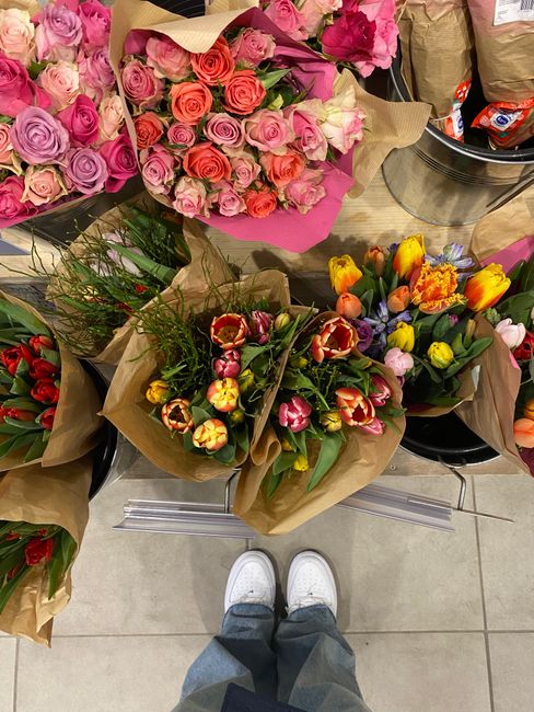A display of vibrant floral arrangements and bouquets in a florist shop, featuring a variety of fresh flowers including pink, purple, and peach roses arranged in large bundles, and tulips with a mix o
